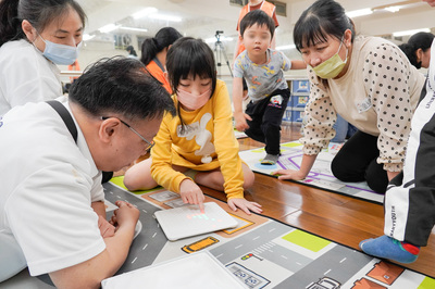 社團法人中華民國遊戲協會理事長林君英(左1)向孩子示範玩具的玩法 家長在一旁學習