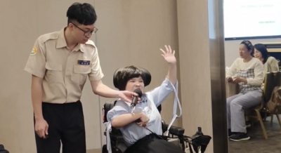  八里愛心教養院院生翁彥如在替代役男林嘉宏(左)的熱心協助下，到台北民樂扶輪社例會中演講。